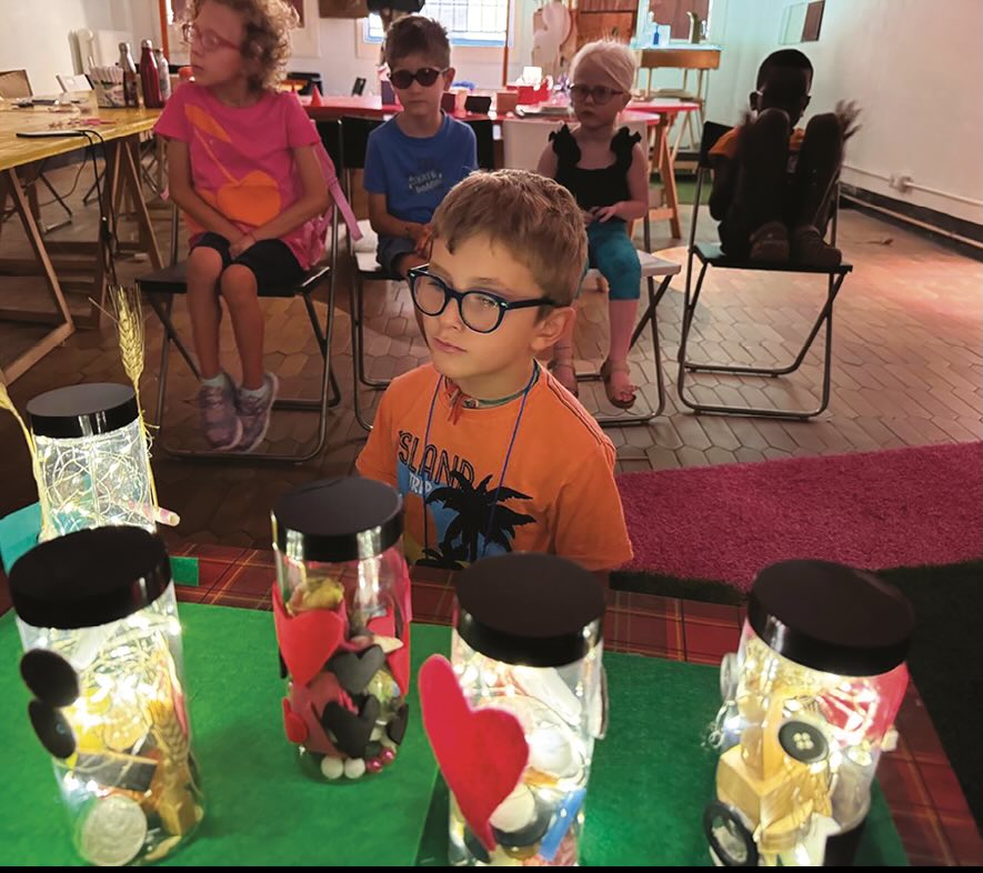 Bambini seduti e bambino in piedi che osserva i barattoli pieni delle loro storie Bambini seduti e bambino in piedi che osserva i barattoli pieni delle loro storie