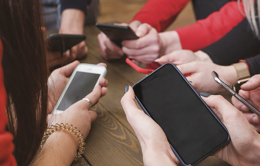Gruppo di mani appoggiate su un tavolo che stringono tutte un cellulare